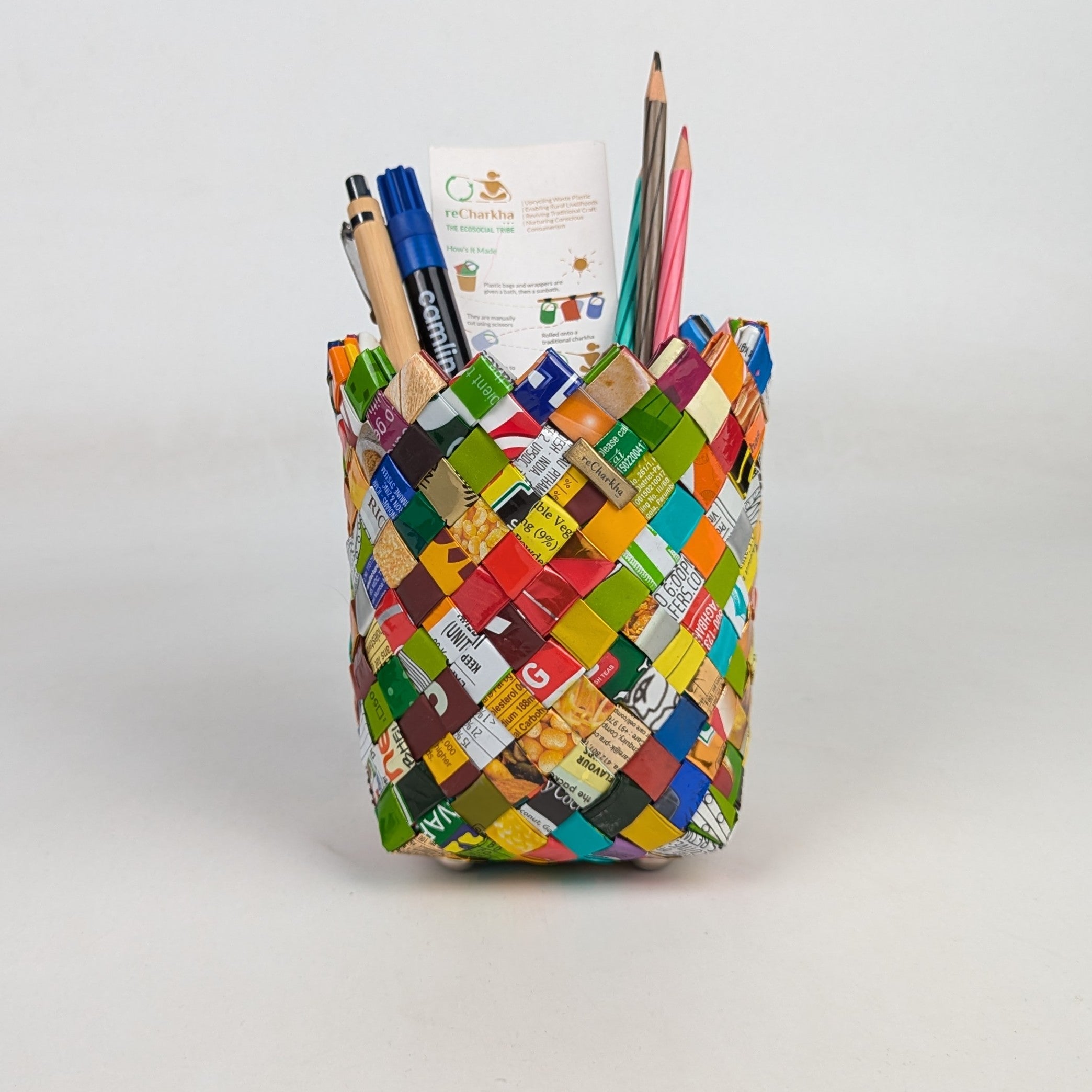 Colorful woven pencil holder with stationery items on a white background