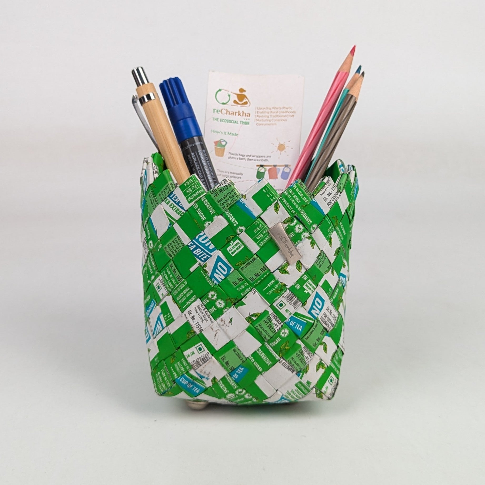 Pencil holder made from recycled green and white boxes with stationery items on a white background