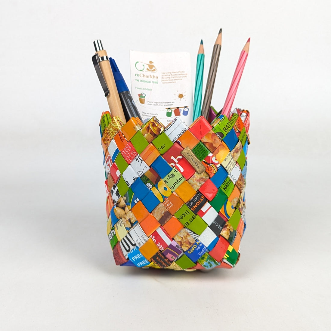 Colorful woven pencil holder with stationery items on a white background